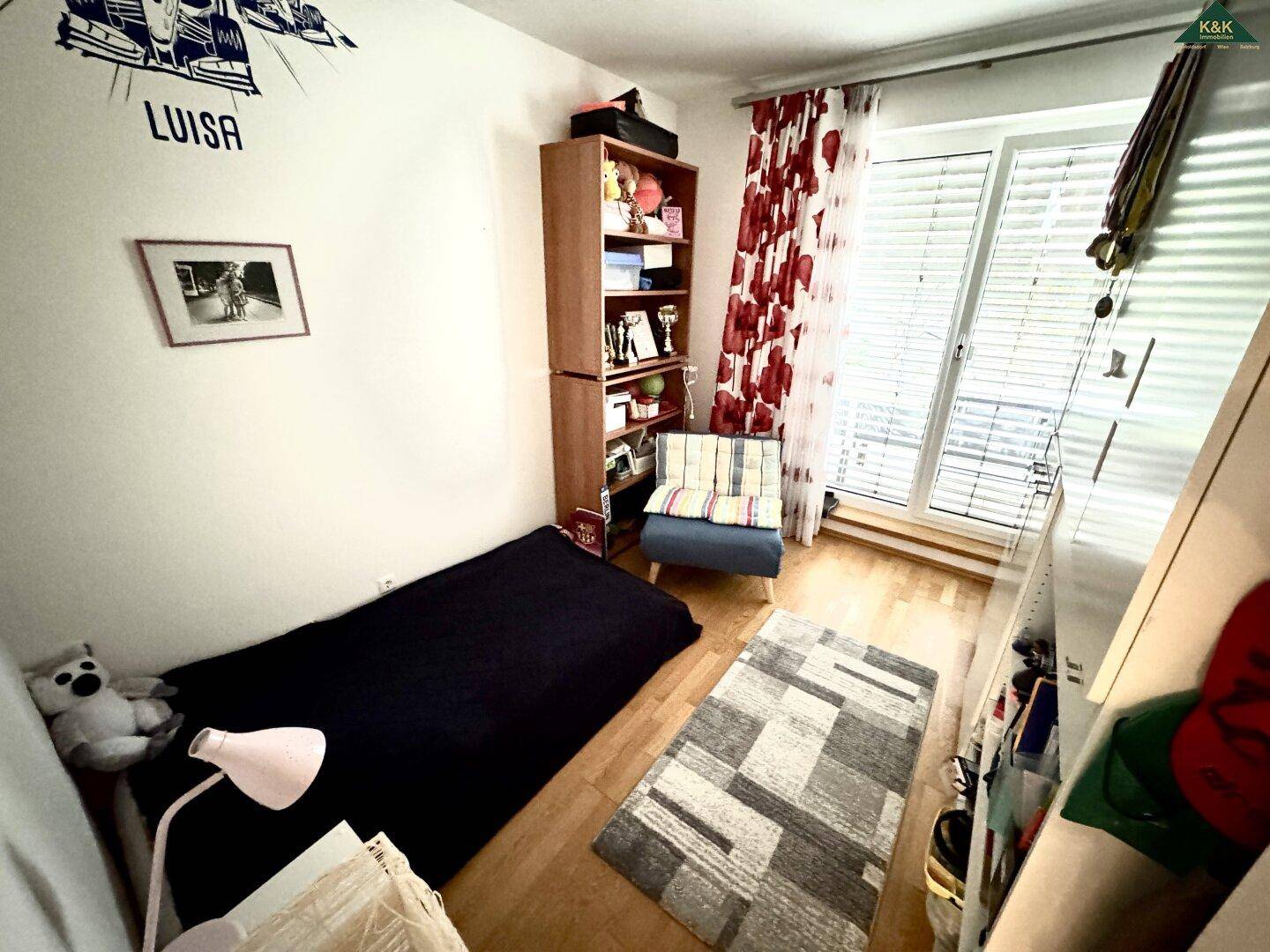 Gemütliches Schlafzimmer mit Einzelbett, Regal und Fenster mit Jalousien auf Holzboden.