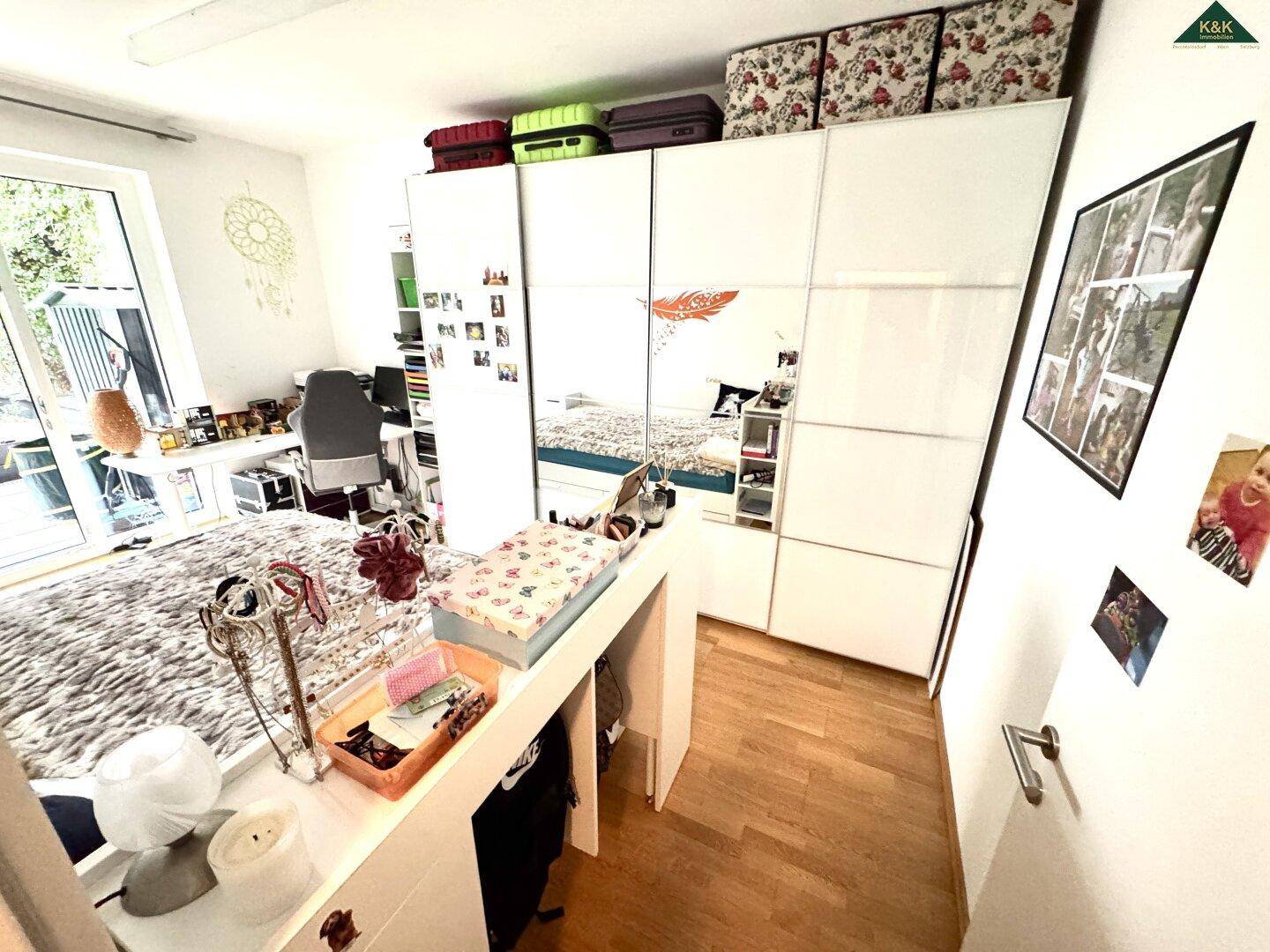 Helles Schlafzimmer mit Doppelbett, Spiegelschrank und Schreibtischbereich, mit Zugang nach draußen.