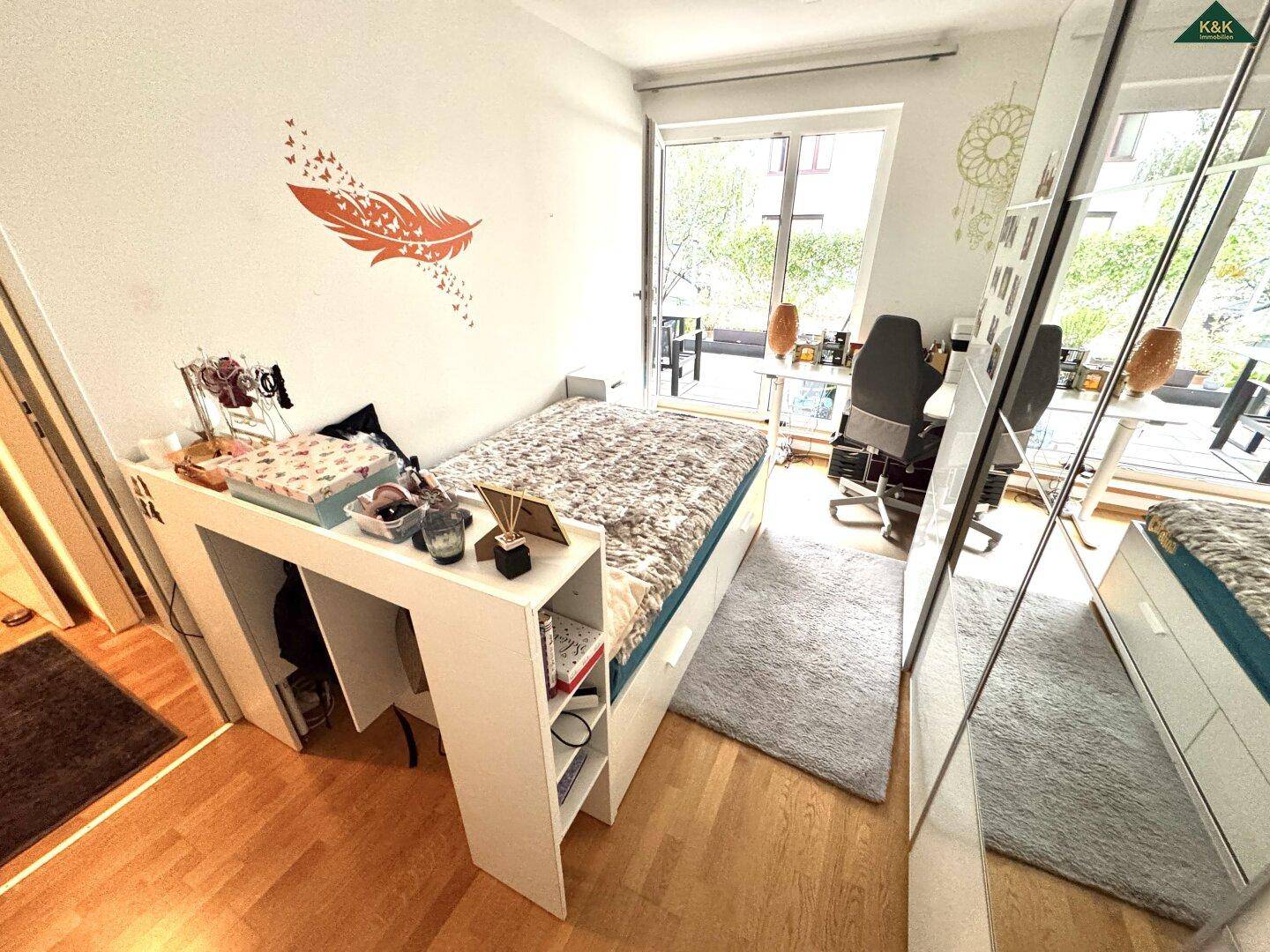 Schlafzimmer mit Bett, Schreibtisch und großem Spiegelschrank, der den Raum optisch vergrößert.
