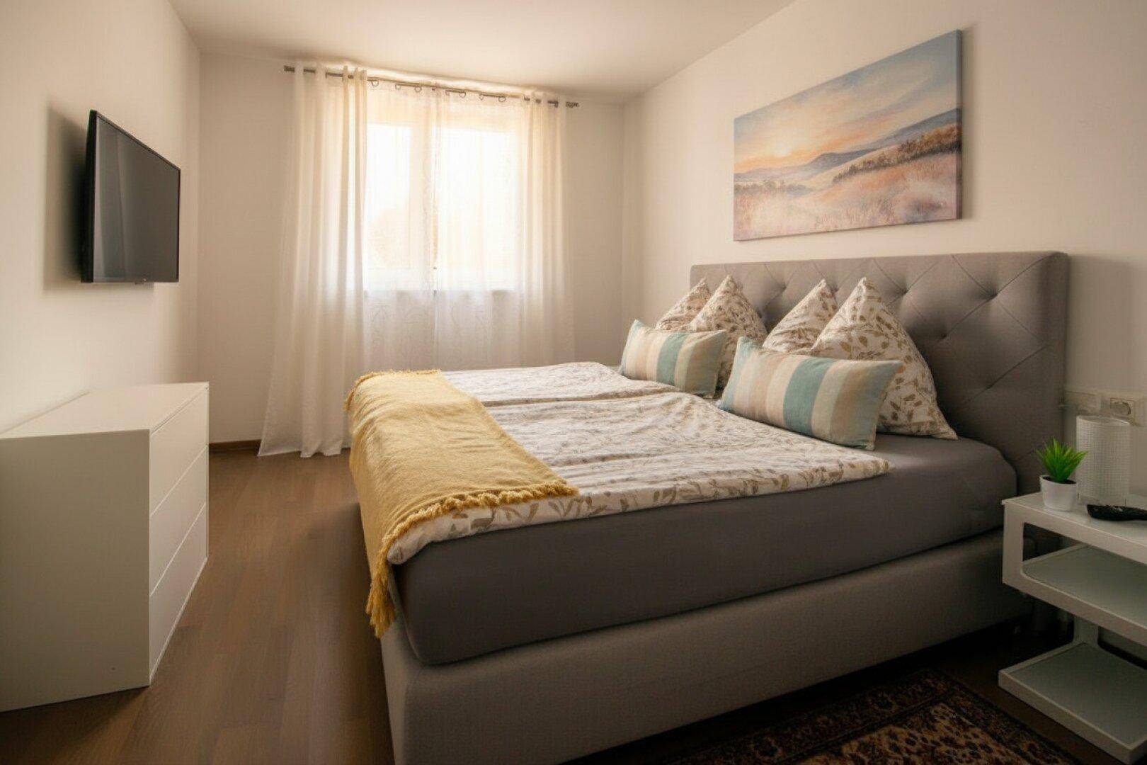 Helles Schlafzimmer mit großem Doppelbett, Holzboden und einem Fenster für viel Tageslicht.