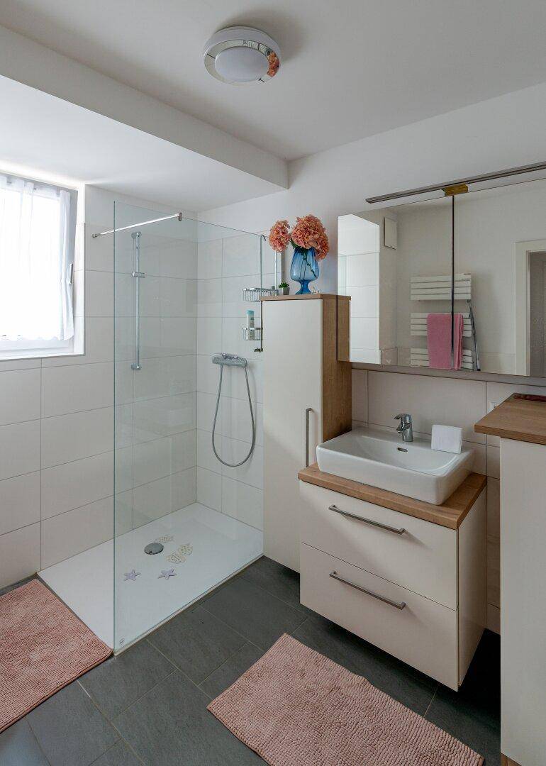 Modernes Badezimmer mit ebenerdiger Dusche, Fenster und Waschtisch mit Unterschrank.