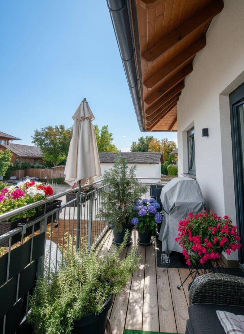 Sonniger Balkon mit Holzboden, Pflanzen, Grill und Sitzgelegenheiten für entspannte Stunden.