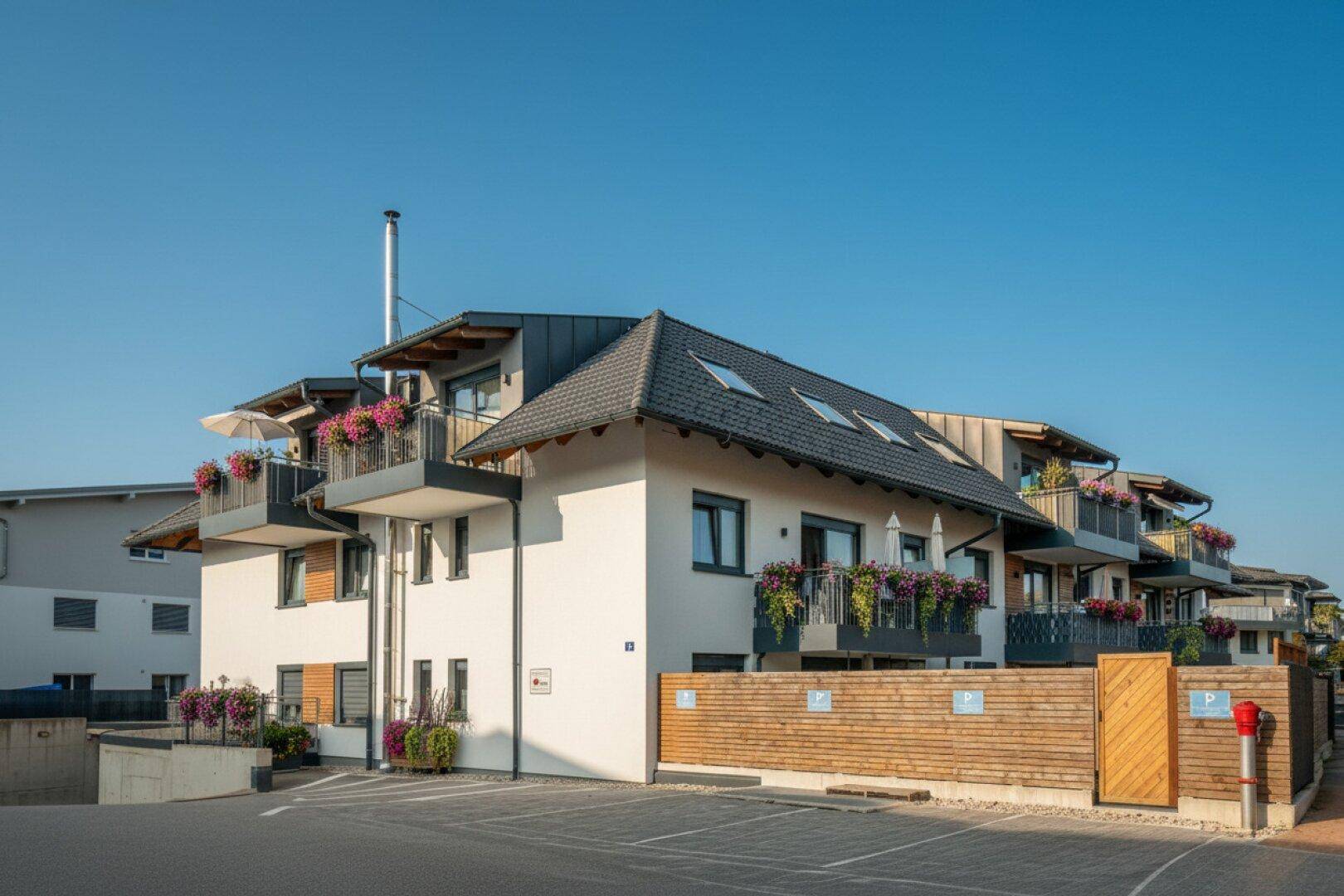 Moderne Wohnanlage mit weißer Fassade, Balkonen und Satteldach unter blauem Himmel.