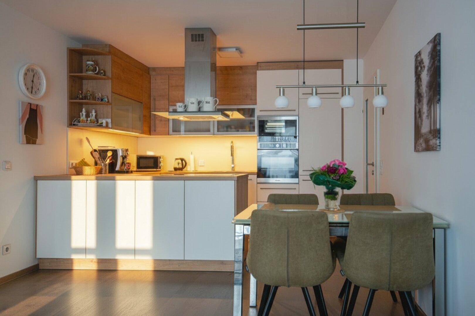 Moderne Einbauküche mit Holzelementen und Essbereich, beleuchtet von warmem Sonnenlicht.