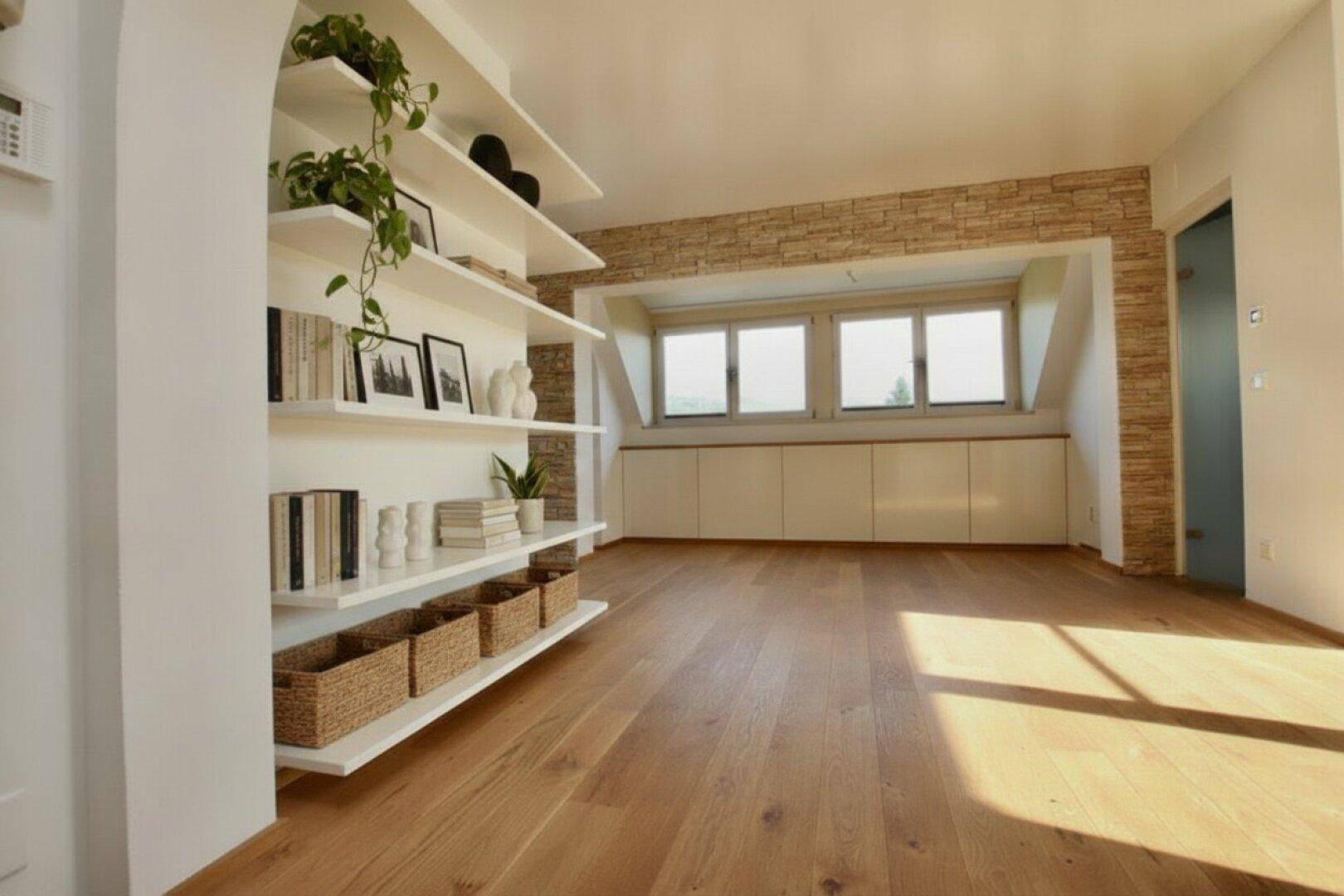 Geräumiger Wohnbereich mit Holzboden, Steinwand und großen Fenstern, ideal für individuelle Gestaltung.