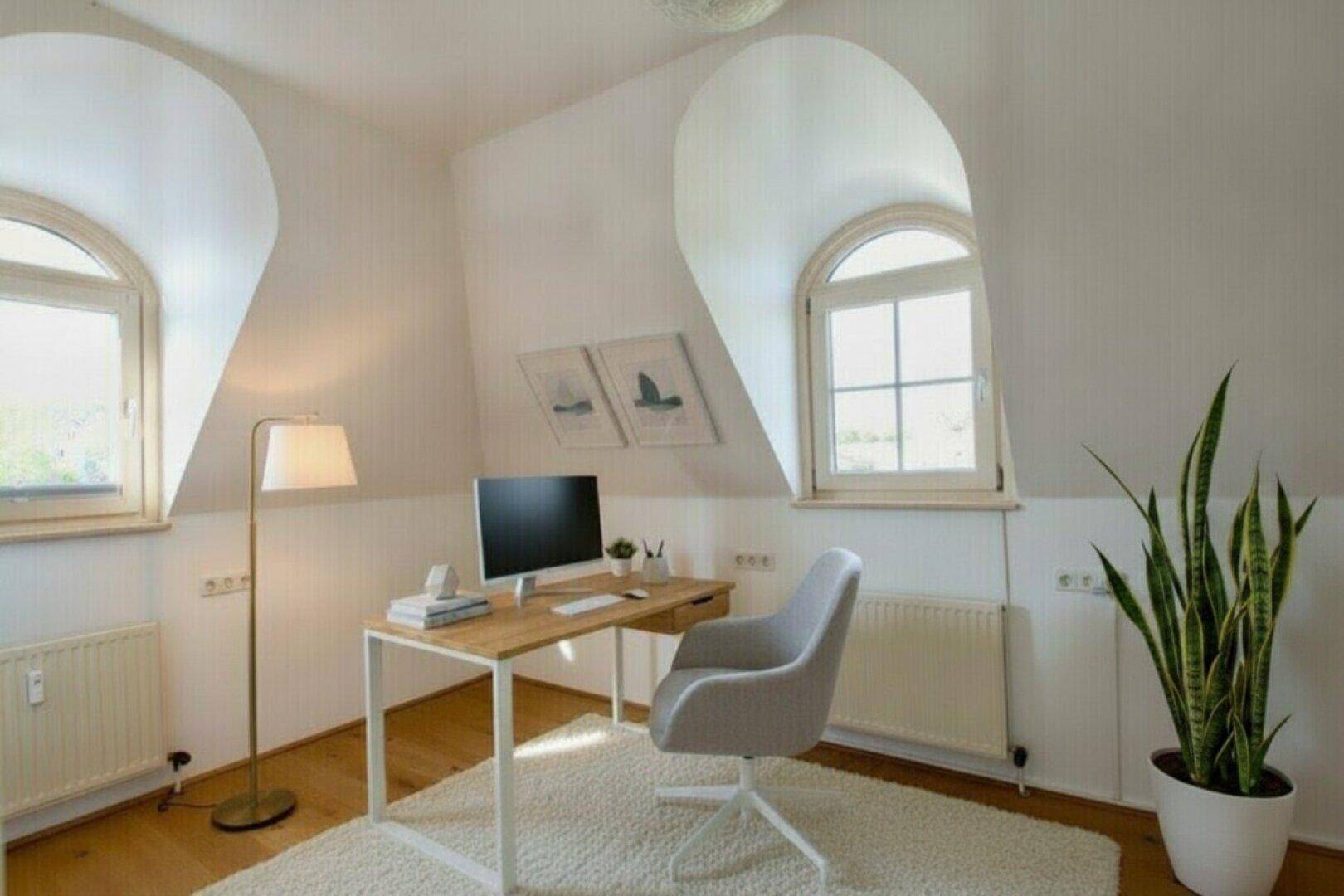 Helles Arbeitszimmer mit modernem Schreibtisch, Bürostuhl und zwei Rundbogenfenstern.