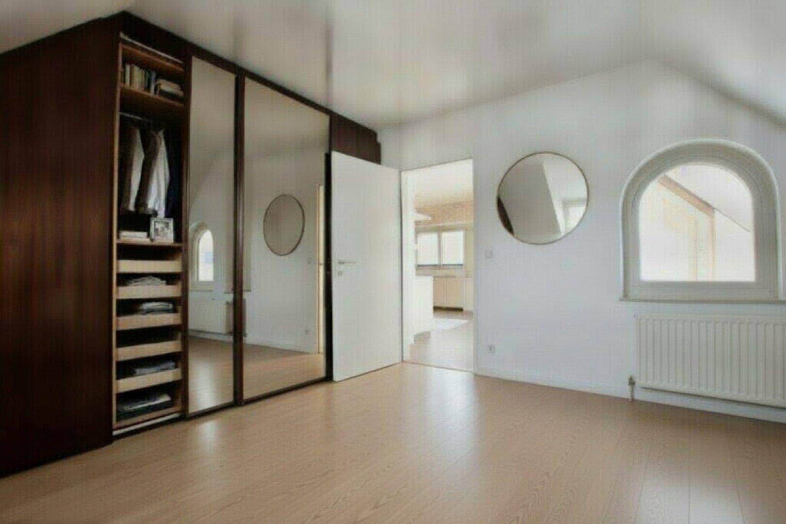 Schlafzimmer mit Holzboden, großem Spiegelschrank und Rundbogenfenster, das viel Licht spendet.
