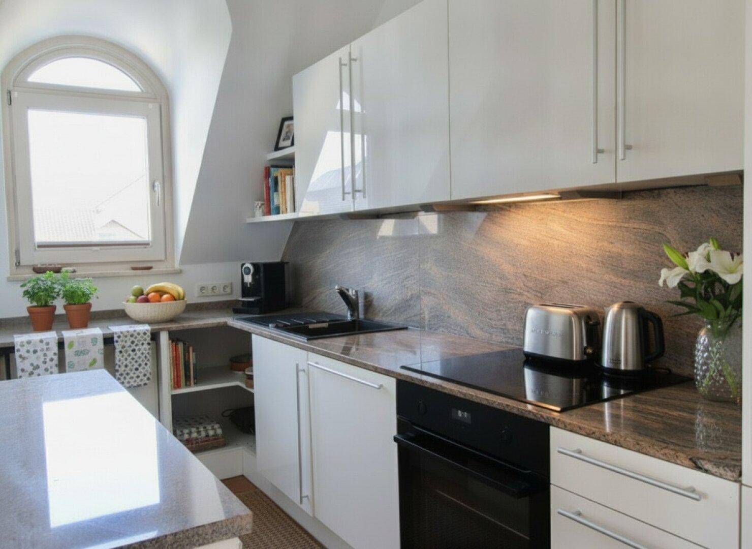 Moderne Küche mit weißen Hochglanzschränken, Granitarbeitsplatten und Induktionskochfeld.