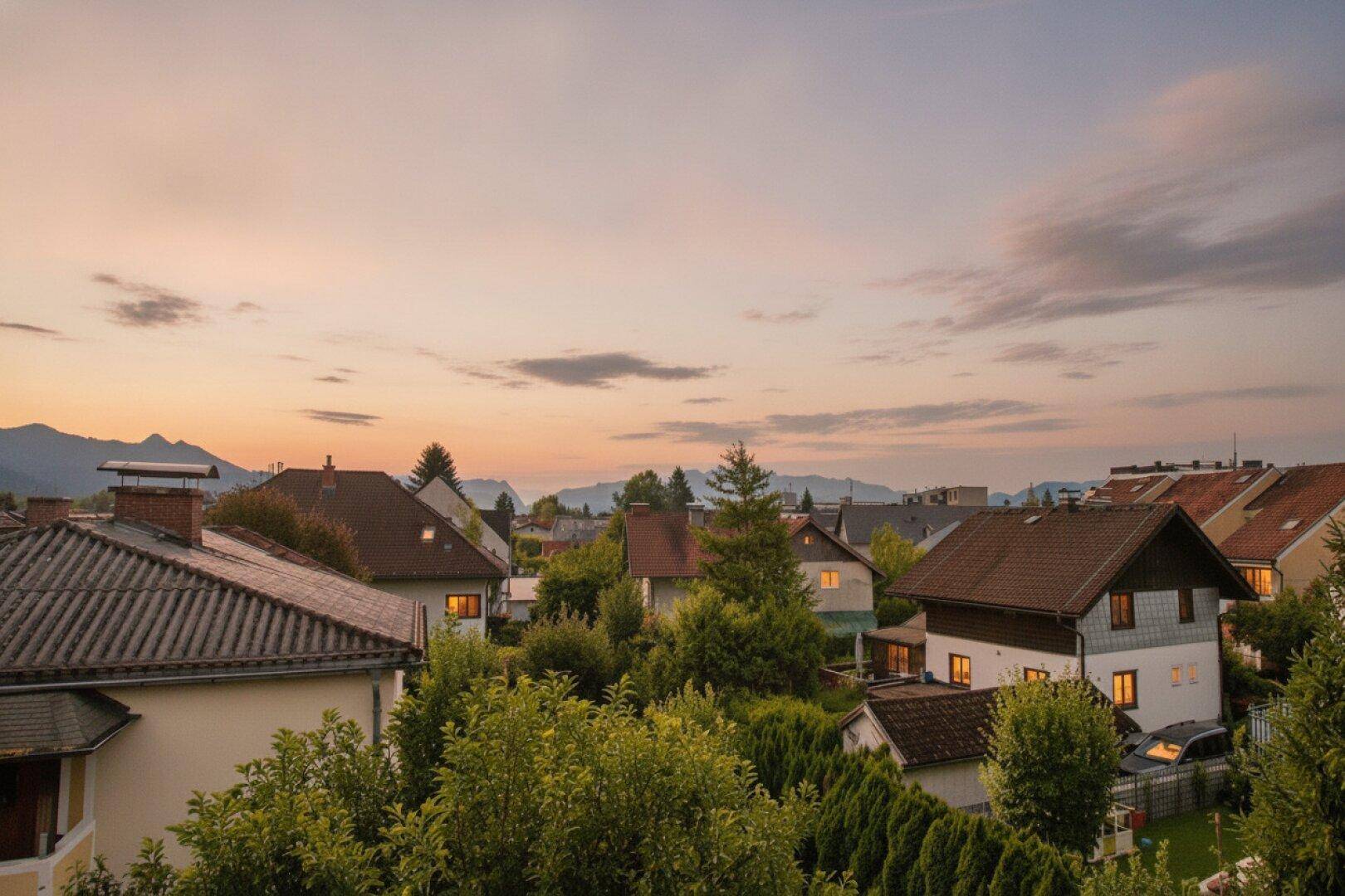 Abendlicher Blick über eine ruhige Wohngegend mit beleuchteten Häusern und Bergen im Hintergrund.