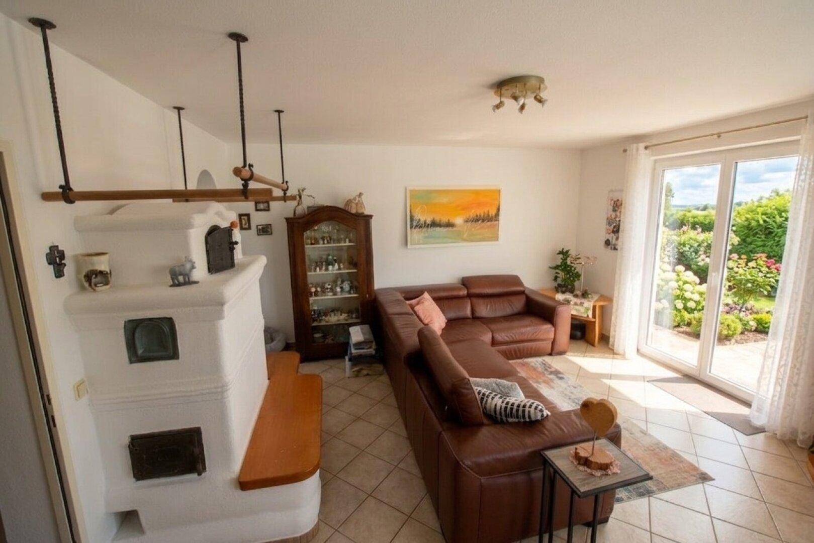 Wohnzimmer mit traditionellem Kachelofen, Ledersofa und direktem Zugang zum Garten.