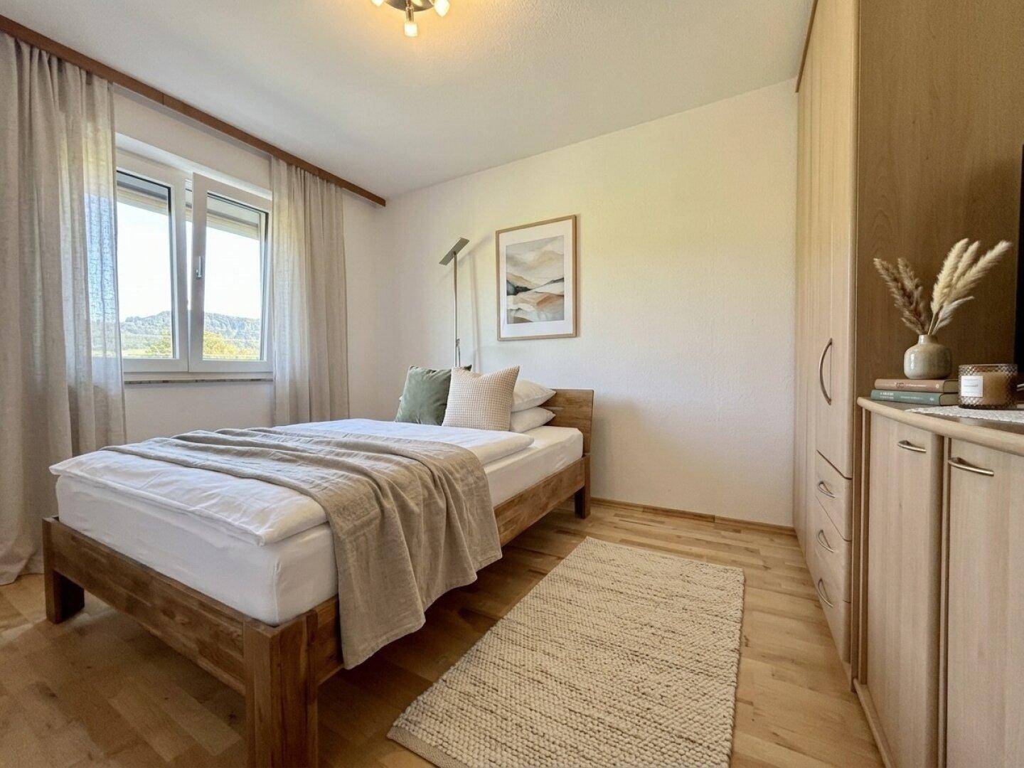 Helles Schlafzimmer mit Holzbett, Kleiderschrank und Blick auf die umliegende Landschaft.