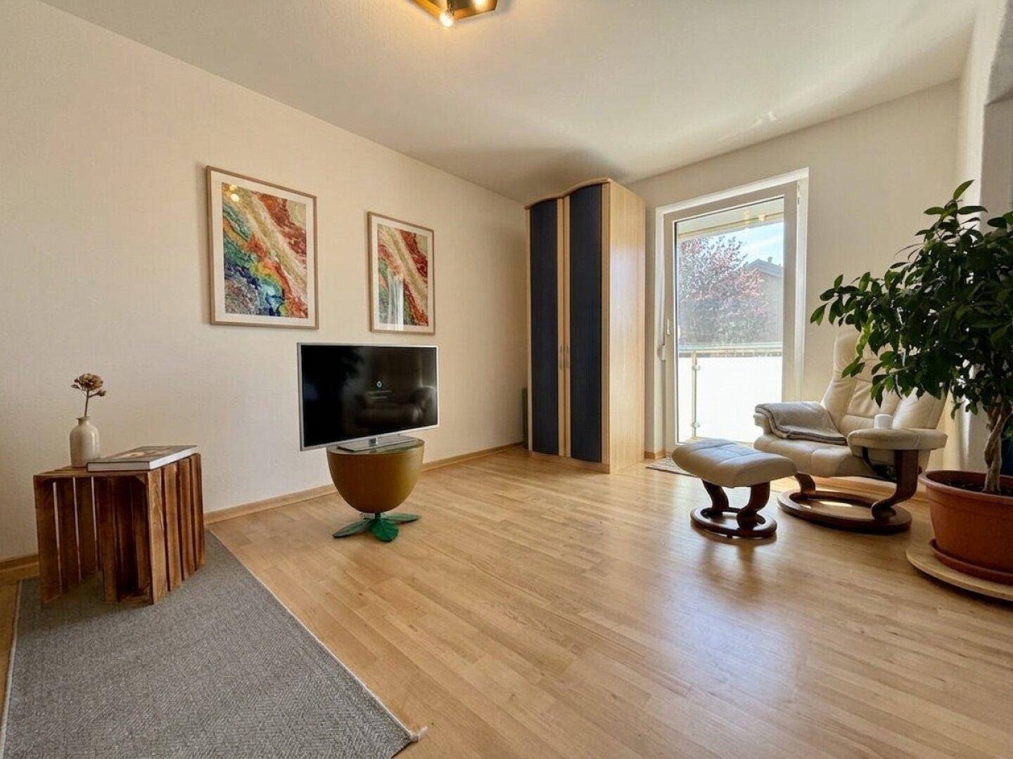 Helles Zimmer mit Holzboden, Sessel und Zugang zu einem kleinen Balkon.