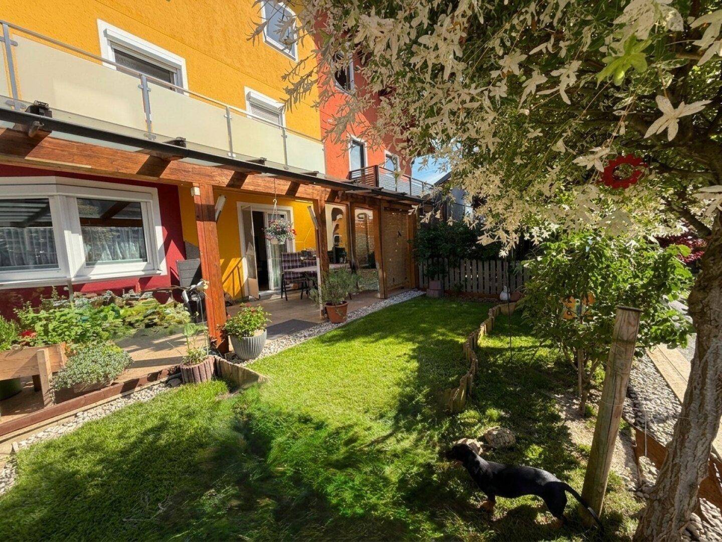 Gepflegter Gartenbereich mit Rasenfläche, überdachter Terrasse und Sitzgelegenheiten.