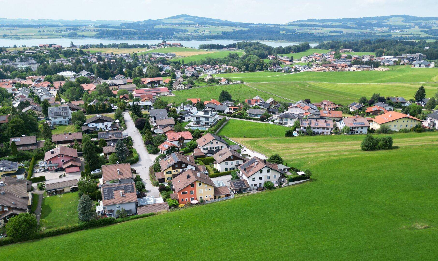 Weitläufige Luftaufnahme der Wohnsiedlung mit grünen Feldern und einem See im Hintergrund.