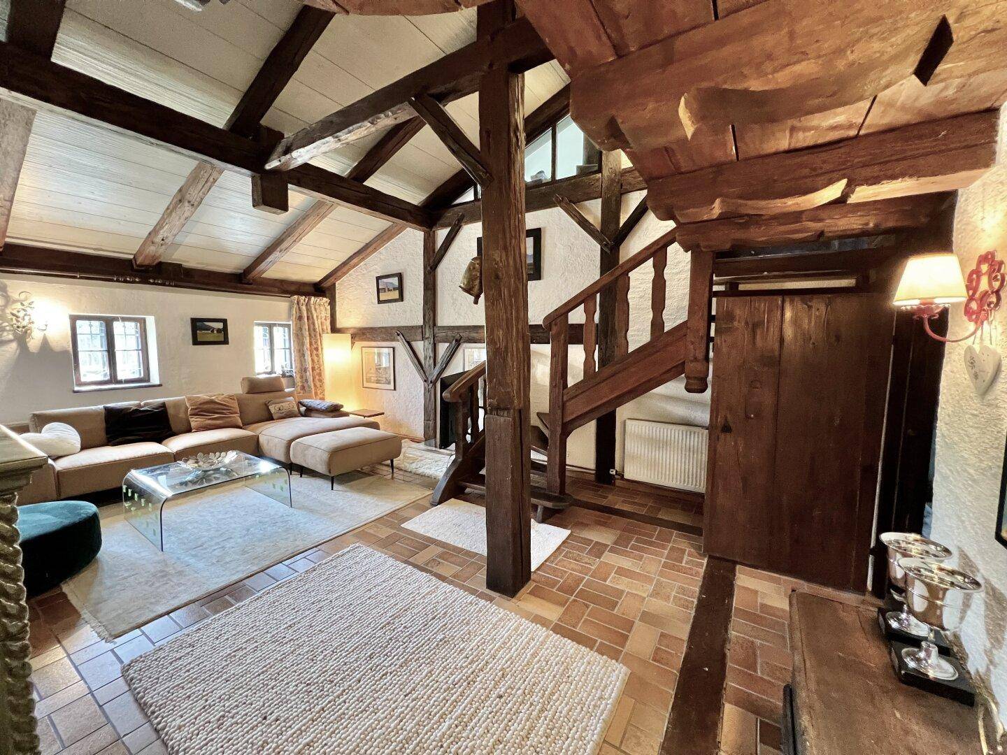 Gemütliches Wohnzimmer mit sichtbaren Holzbalken, rustikalem Charme und einer Holztreppe.