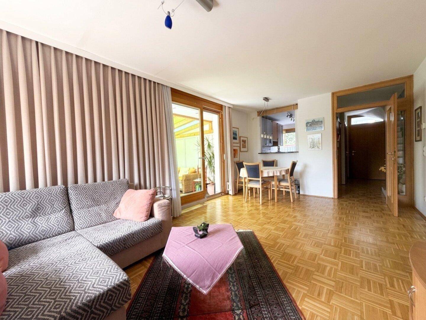 Geräumiger Wohn-Essbereich mit Parkettboden, gemütlichem Sofa und Zugang zu einem Wintergarten.