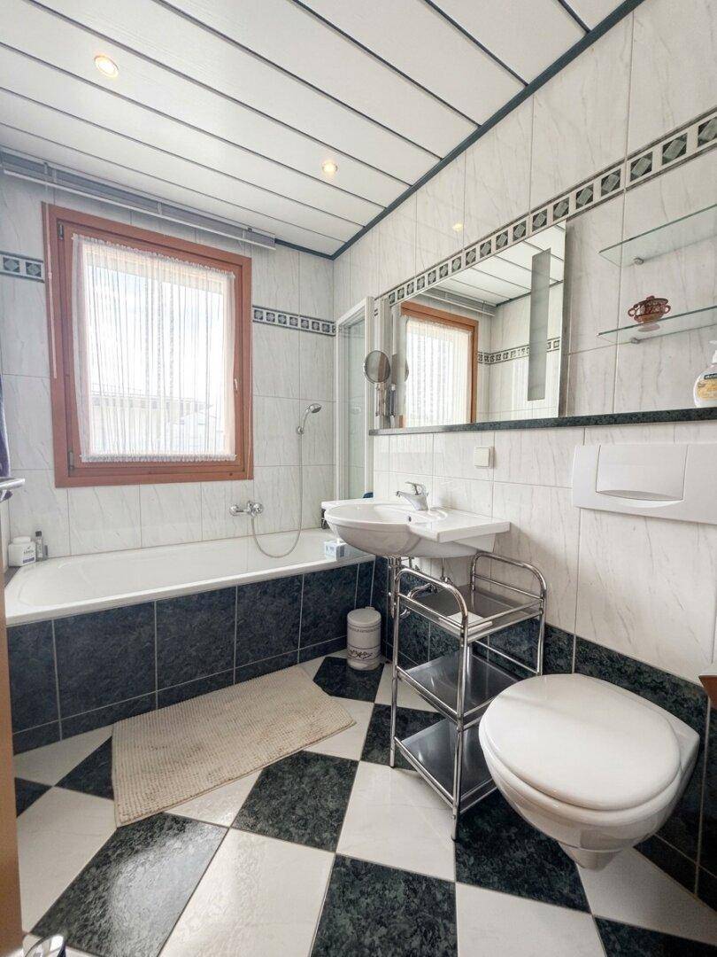 Gefliestes Badezimmer mit Badewanne, Duschbereich und Fenster für Tageslicht.