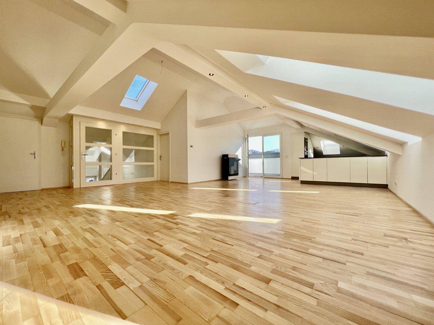 Heller, offener Wohnbereich im Dachgeschoss mit Holzboden, Dachfenstern und Zugang zur Terrasse.