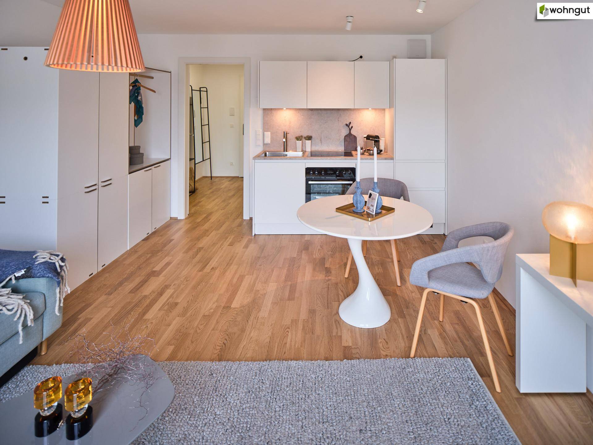 Heller Wohnbereich mit integrierter Küchenzeile, Sofa und Holzboden.