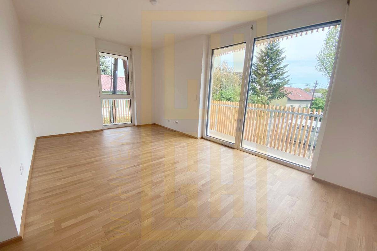 Heller Raum mit Parkettboden und großen Fenstern, die Zugang zu einem Balkon bieten.