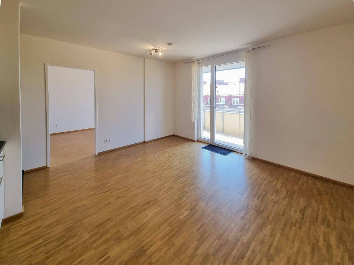 Heller Wohnbereich mit Parkettboden und Zugang zum sonnigen Balkon.