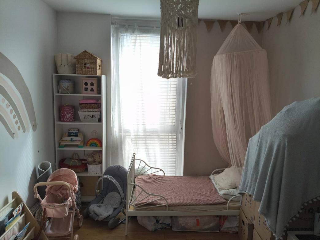 Kinderzimmer mit Einzelbett, Bücherregal und einem großen Fenster mit Jalousien.