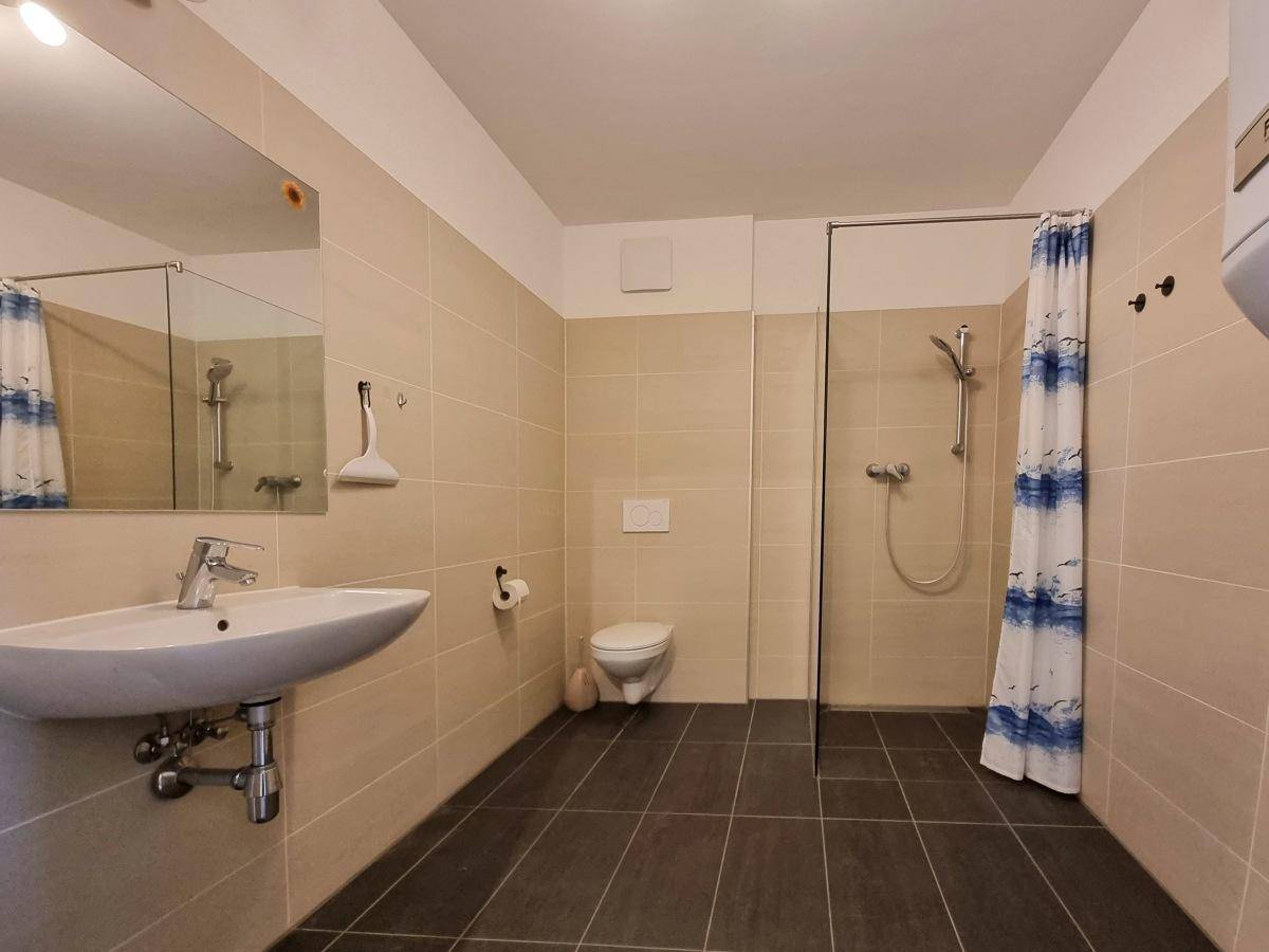 Modernes Badezimmer mit beigefarbenen Fliesen, Dusche und Wand-WC.