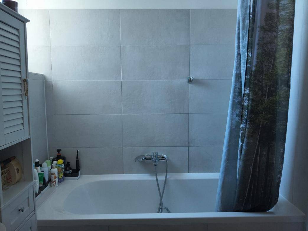 Badezimmer mit Badewanne, Duschvorhang und hellgrauen Fliesen an den Wänden.