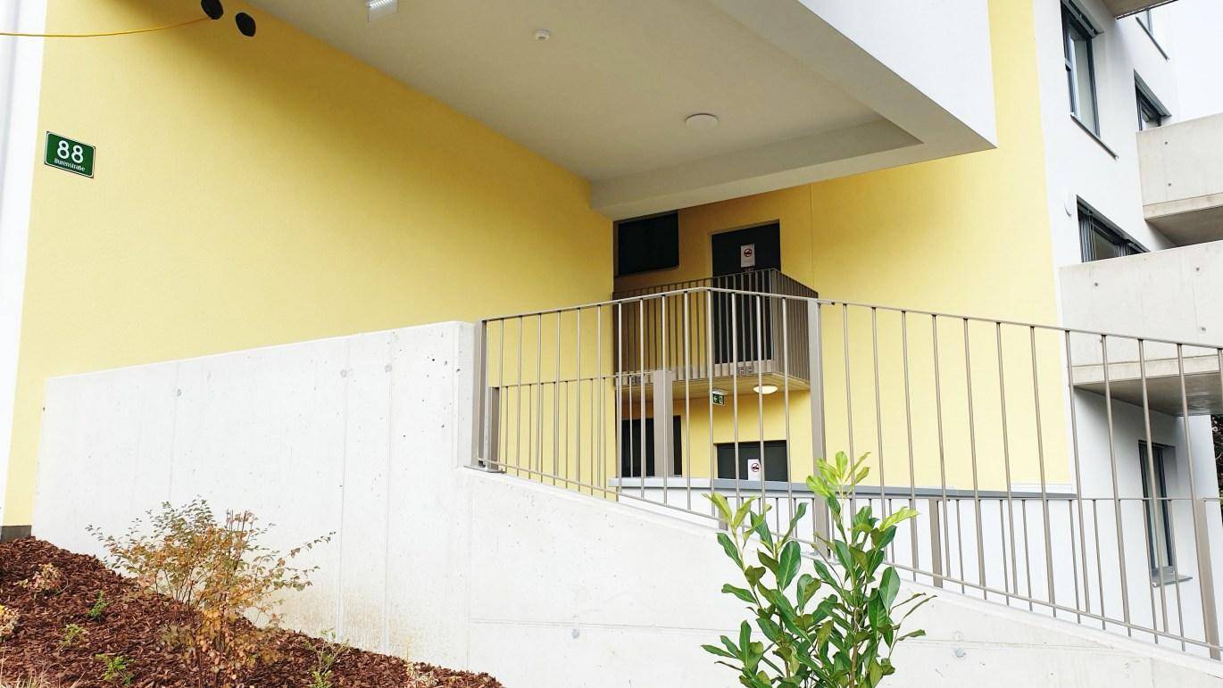 Barrierefreier Eingangsbereich des Neubaus mit gelber Fassade und einer Zugangsrampe.