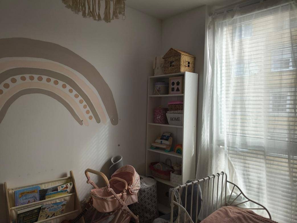 Helles Kinderzimmer mit einem Bücherregal, Spielzeug und einem großen Fenster.