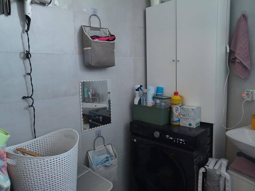Badezimmer mit Waschmaschine, Schrank und einem kleinen Waschbecken.