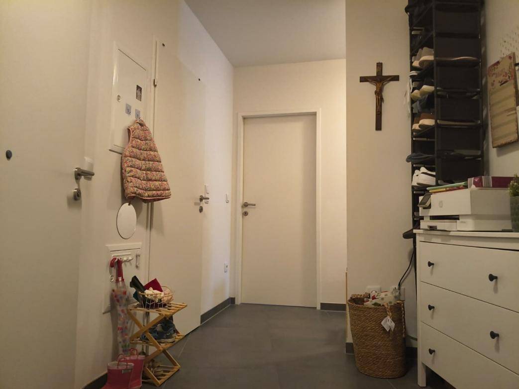 Heller Eingangsbereich mit dunklen Fliesen, Garderobe und einer weißen Tür.
