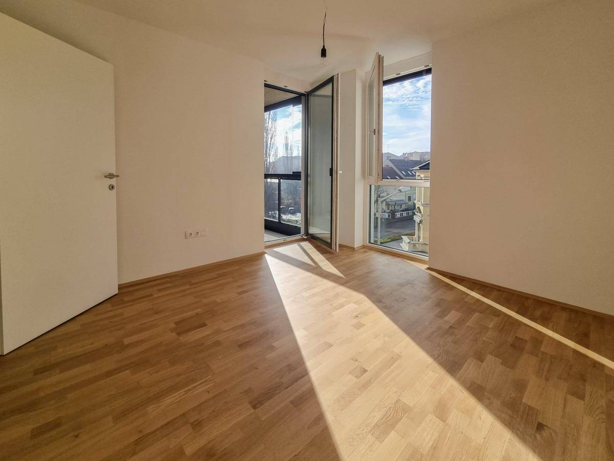 Helles Schlafzimmer mit Holzboden und Zugang zu einem Balkon oder einer Loggia.