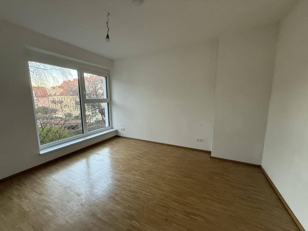 Helles Schlafzimmer mit Parkettboden und einem großen Fenster mit Blick ins Grüne.