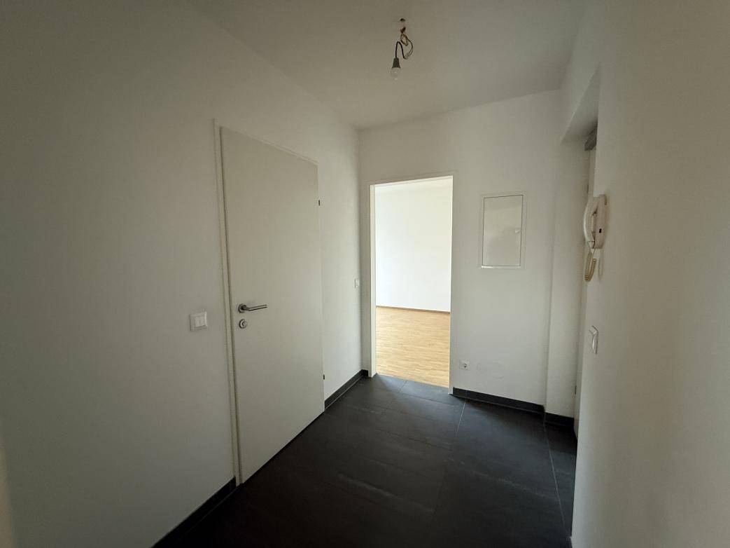 Heller Eingangsbereich mit dunklen Fliesen und einer weißen Tür, die in die Wohnung führt.