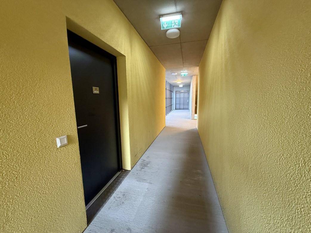 Heller Flur im Gebäude mit gelben Wänden und Betonboden, der zu den Wohneinheiten führt.