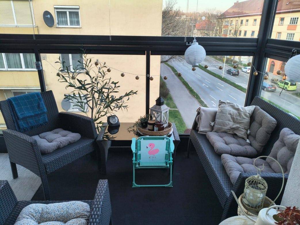 Verglaste Loggia mit bequemen Outdoor-Möbeln und Blick auf die Straße und umliegende Gebäude.