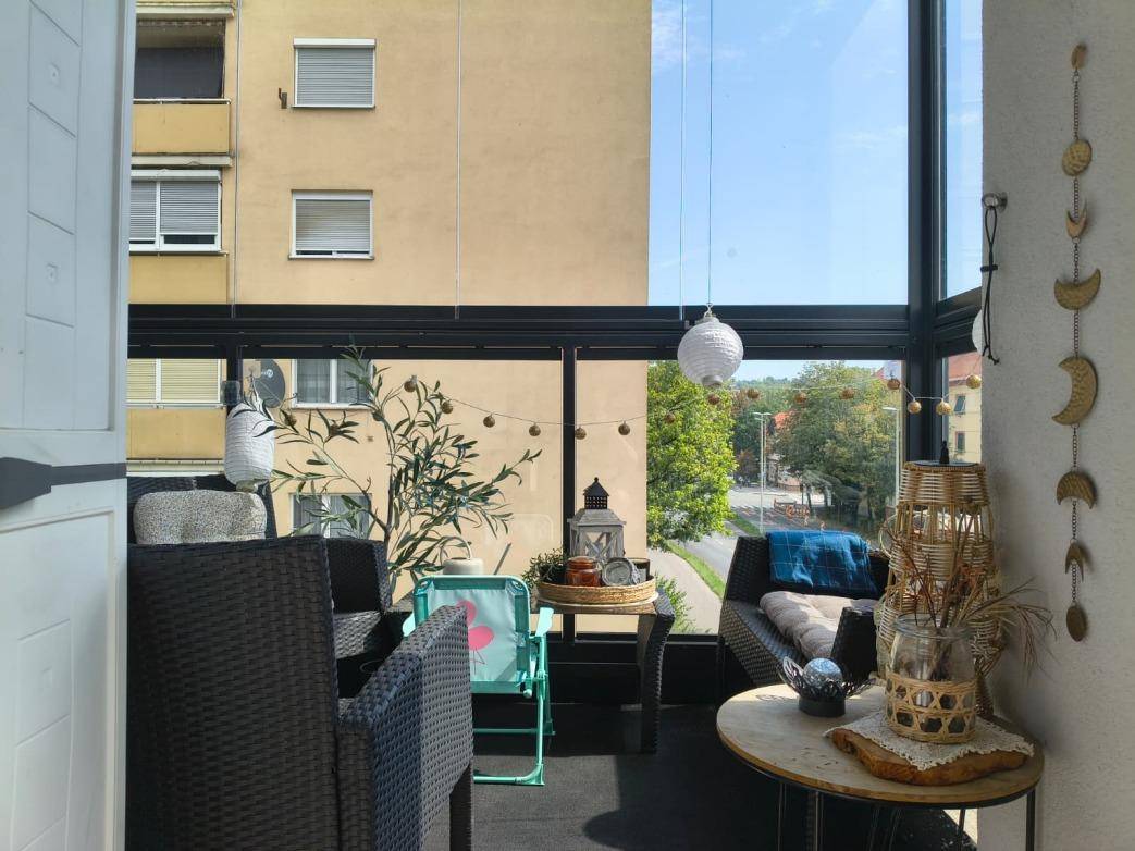 Helle, verglaste Loggia mit Rattanmöbeln und einem Blick auf die grüne Umgebung.