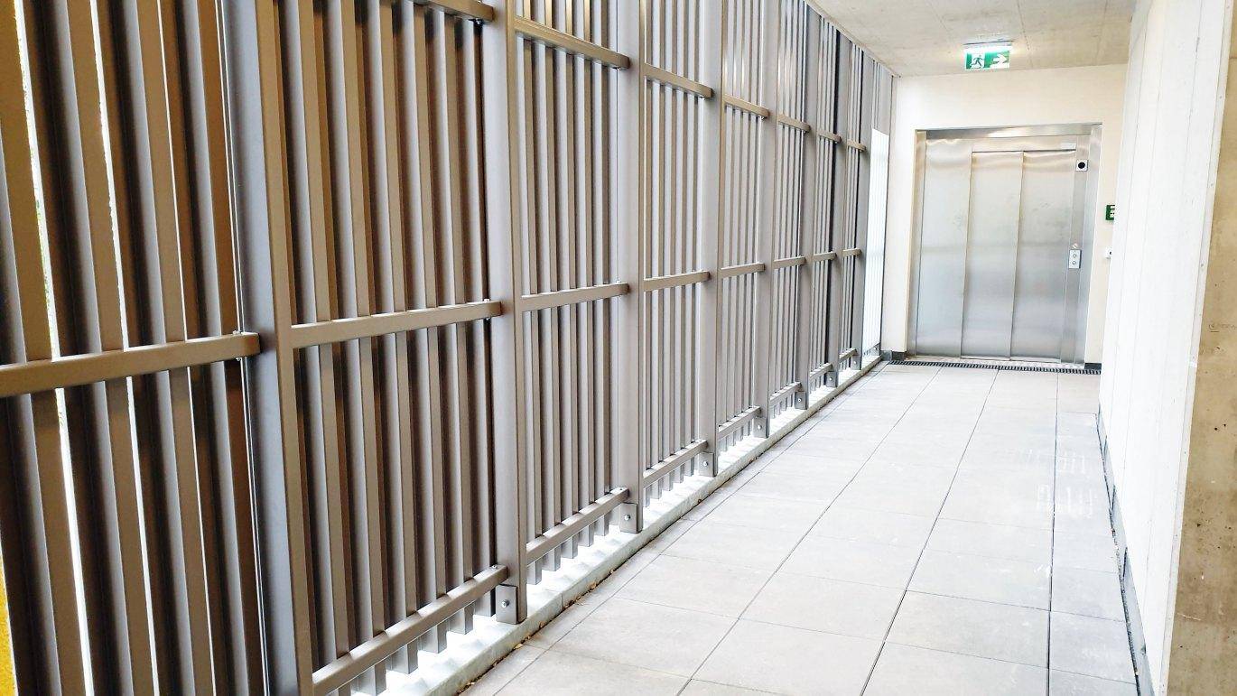 Heller Flur mit Aufzug und modernen Metalllamellen, die für Belüftung sorgen.