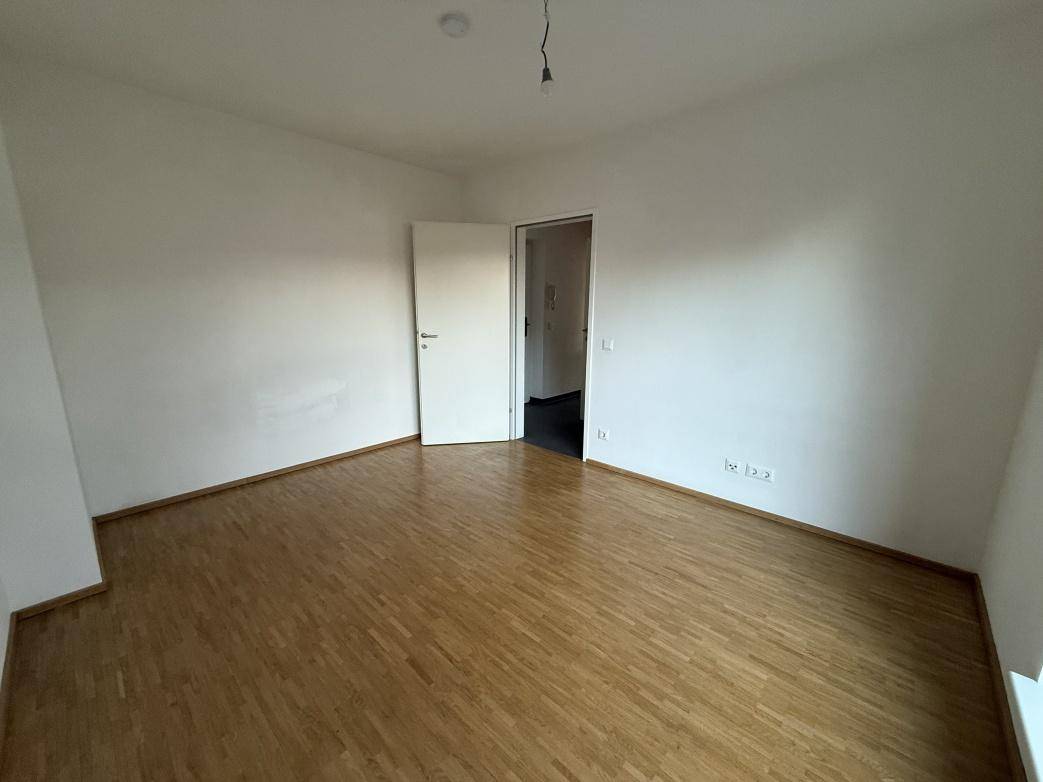 Schlafzimmer mit Holzboden und weißer Tür, die zu einem weiteren Raum führt.