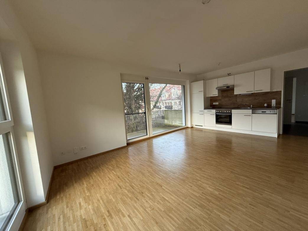 Offener Wohn- und Essbereich mit moderner Einbauküche, Parkettboden und Zugang zum Balkon.