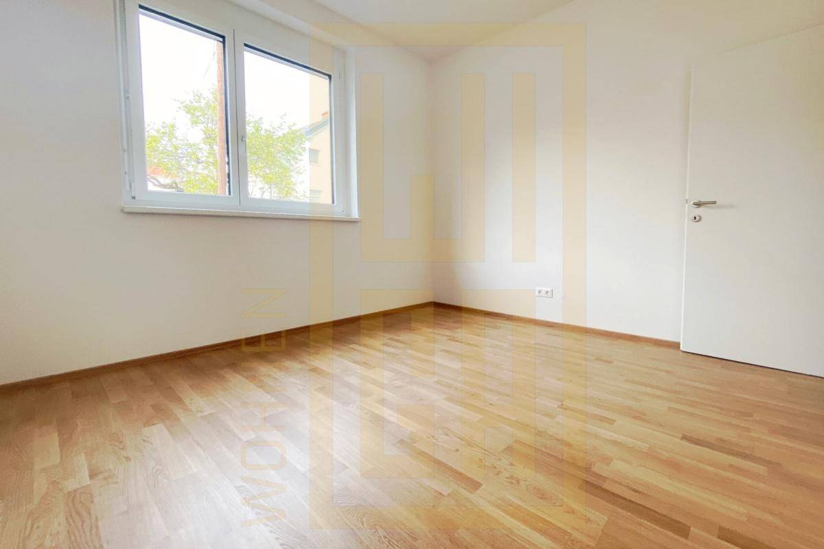 Leeres Zimmer mit hellem Parkettboden und einem Fenster, ideal als Schlaf- oder Arbeitszimmer.