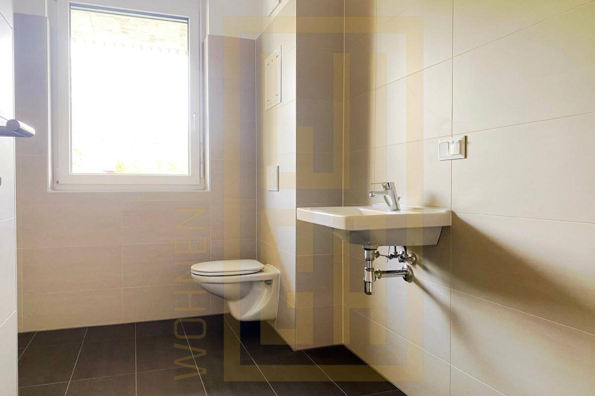 Modernes Badezimmer mit Wand-WC, Waschbecken, Fenster und dunklen Bodenfliesen.