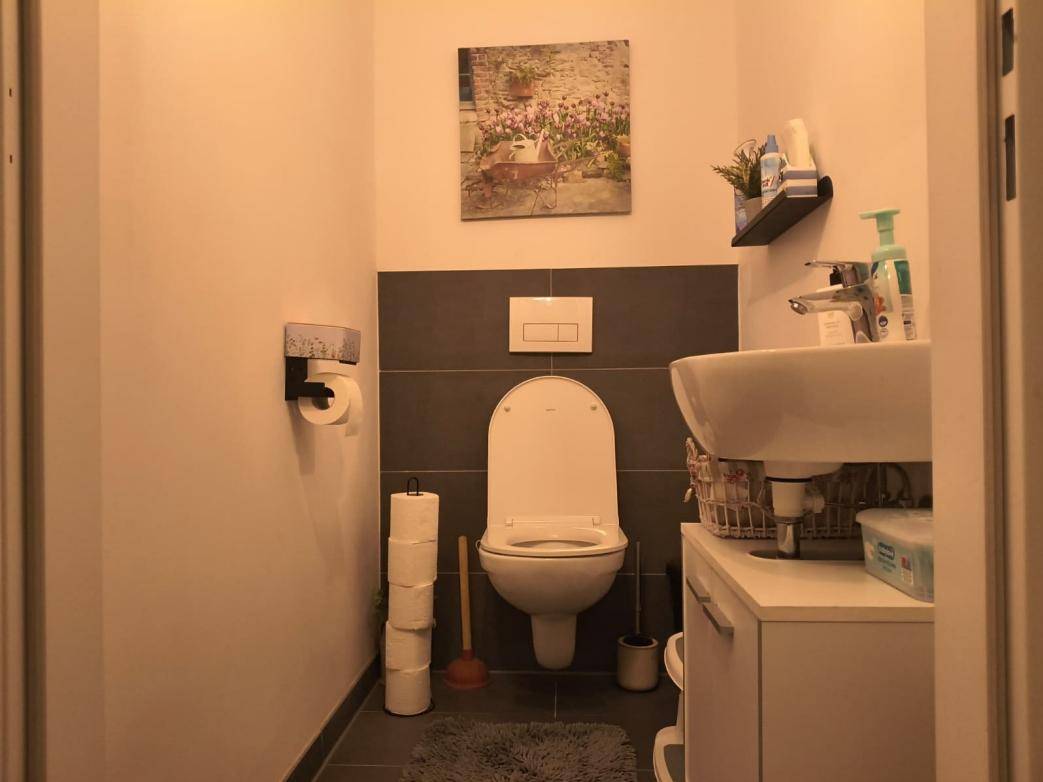 Gäste-WC mit wandhängender Toilette, Waschbecken und einem kleinen Regal.
