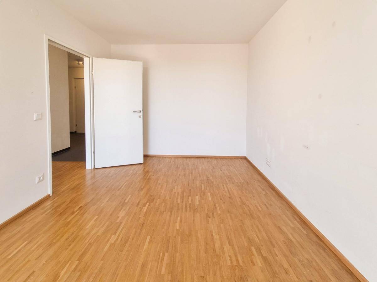 Helles Zimmer mit Parkettboden und weiß gestrichenen Wänden.