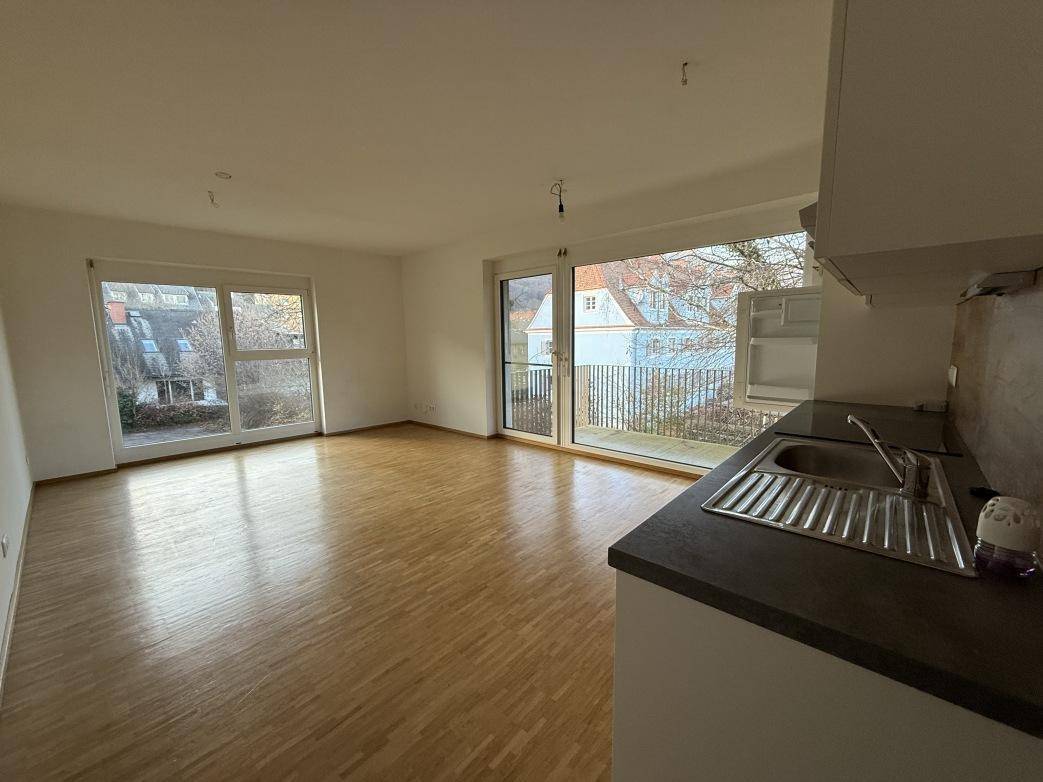 Lichtdurchfluteter Wohnbereich mit Parkettboden, großen Fenstern und einer integrierten Küchenzeile.