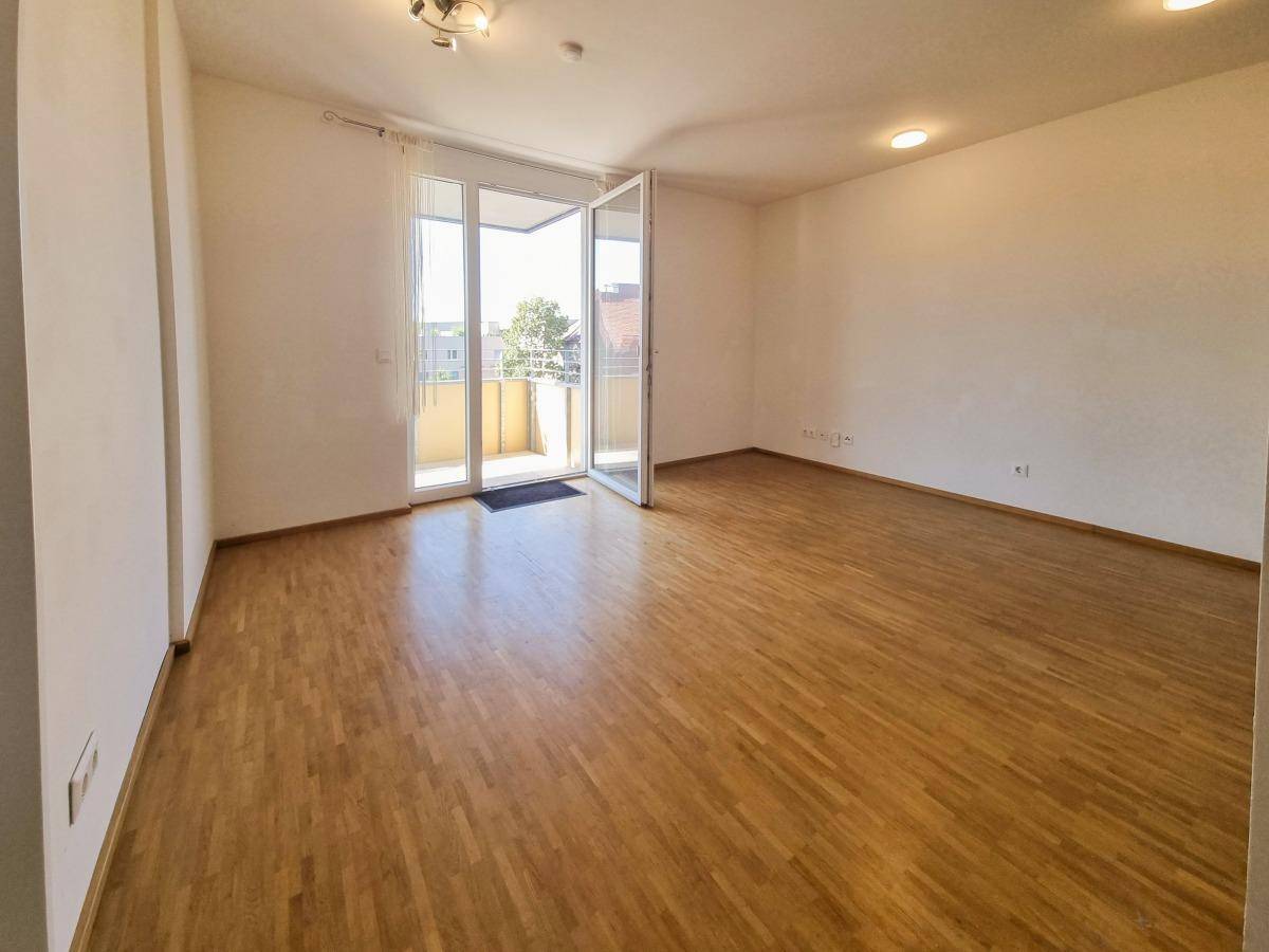 Geräumiger Wohnbereich mit Parkettboden und großen Fenstern zum Balkon.