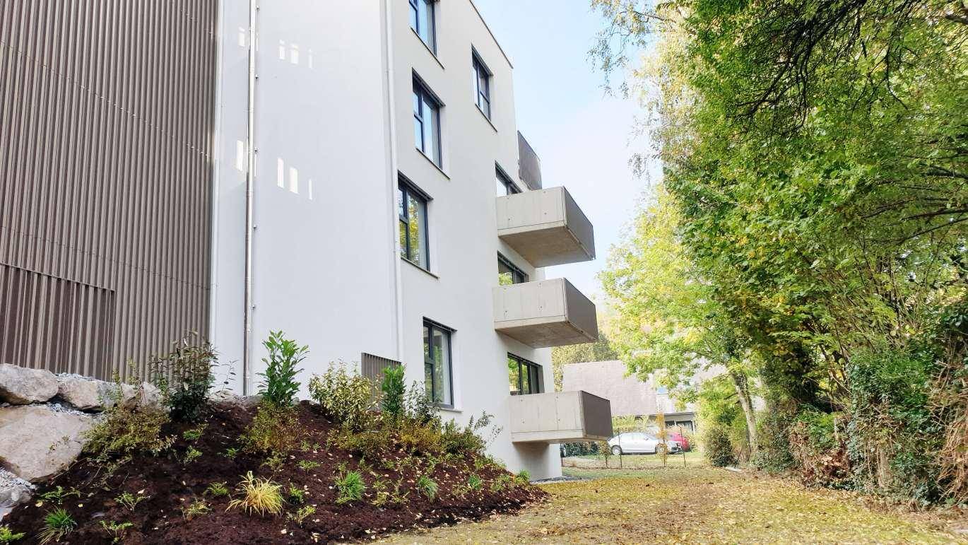 Moderne Gebäudefassade mit mehreren Balkonen, umgeben von üppigem Grün und Bäumen.