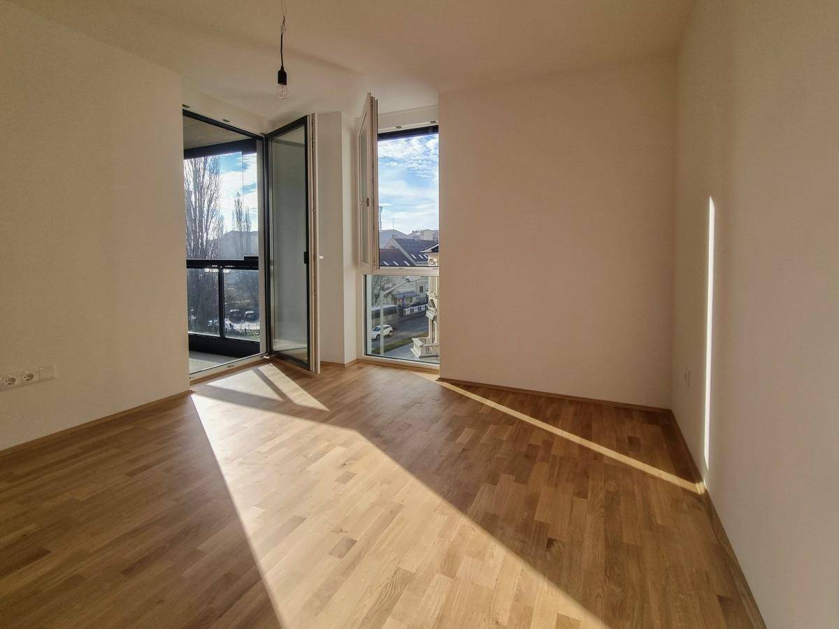 Lichtdurchflutetes Zimmer mit Parkettboden und großen Fenstern mit Stadtblick.