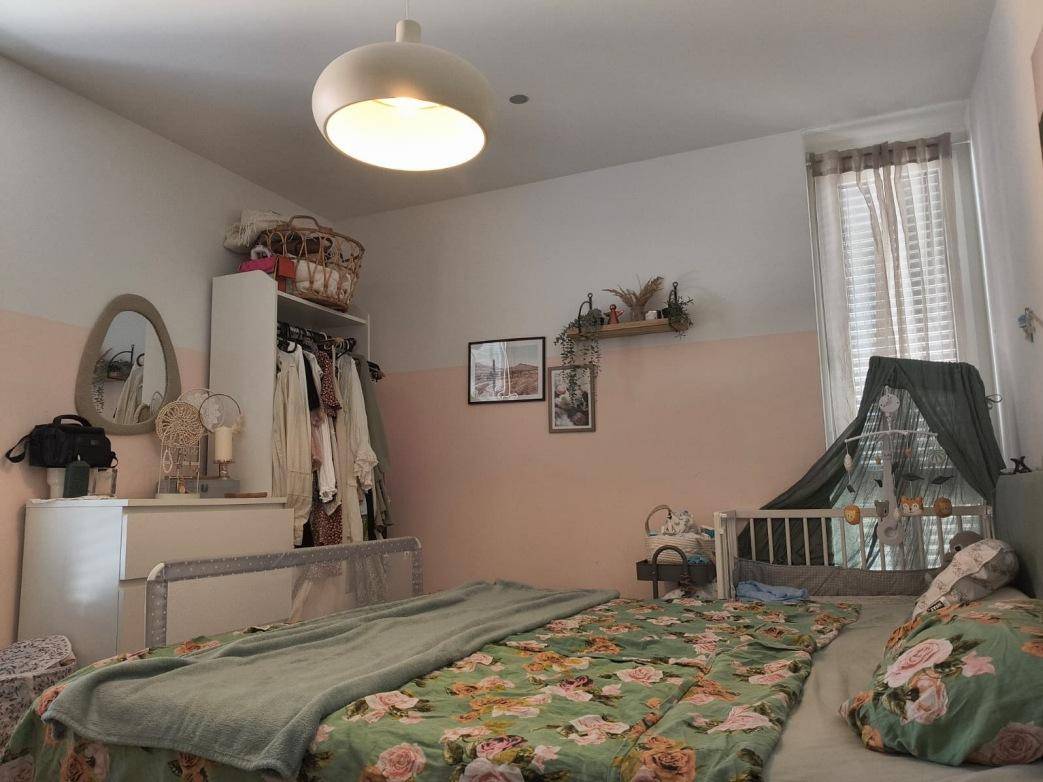 Schlafzimmer mit Doppelbett, Kommode und einem Fenster, das viel Tageslicht hereinlässt.